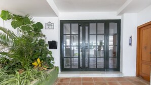 Une entrée moderne avec une porte en verre, un pot de fleurs et une plaque indiquant le numéro de l’immeuble.