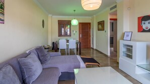 A modern living room with a sofa, a dining table, and a kitchen area in the background. - Balcony with Sea View in Lambda 1 Apartment (Almuñécar)