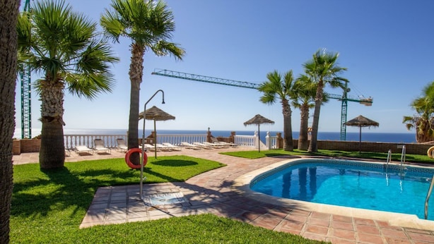 A pool area with palm trees, lounge chairs, and a view of the ocean. - Balcony with Sea View in Lambda 1 Apartment (Almuñécar)