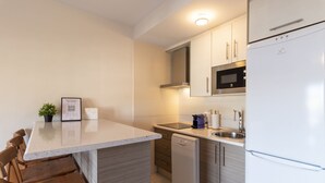 A compact kitchen with a dishwasher, microwave, and refrigerator. There is a small island with chairs and a potted plant. - Incredible Views at Apartment Lambda 2 (Almuñécar)