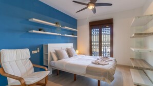 A bedroom with a bed, a chair, a ceiling fan, and a window with a metal gate. - Incredible Views at Apartment Lambda 2 (Almuñécar)