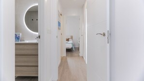 A hallway leading to a bedroom with a bed, a bathroom with a mirror, and a wooden floor.