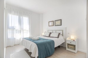Een slaapkamer met een bed, nachtkastjes, een raam met dunne gordijnen en twee ingelijste foto's aan de muur.