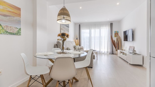 A modern dining area with a round glass table, white chairs, and a hanging light fixture.