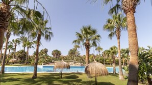 A poolside area with palm trees and thatched umbrellas.