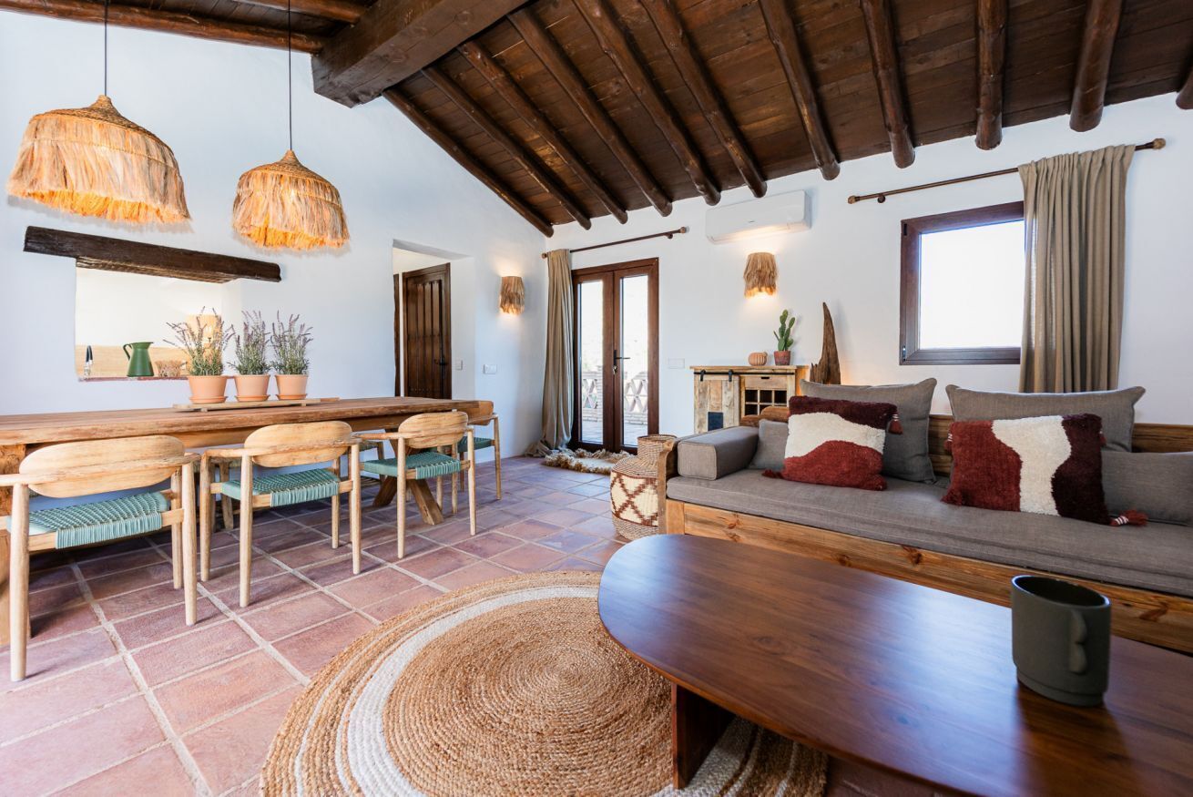 A cozy living room with a wooden sofa, a coffee table, and a dining area with chairs and a table.