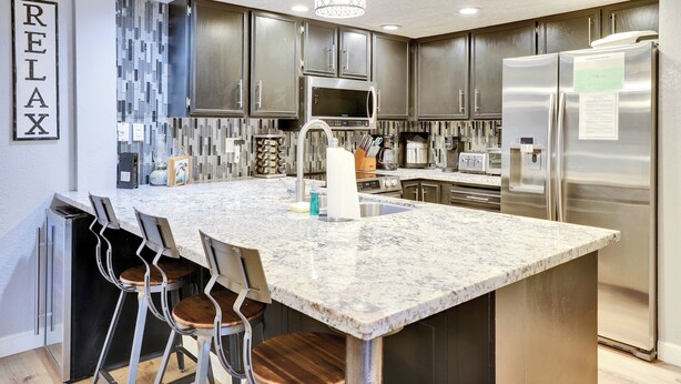 A modern kitchen with a large island, stainless steel appliances, and a 'RELAX' sign on the wall.