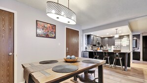 A modern kitchen with dark cabinetry, stainless steel appliances, and a wooden dining table with stools.