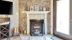 A living room with a stone fireplace, a mounted television, and a door leading outside.