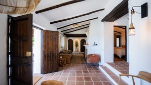 Un couloir au décor rustique, avec des poutres apparentes, un sol carrelé et un coin salon comprenant un canapé et des fauteuils.