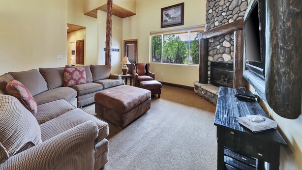 A cozy living room with a stone fireplace, a large window, and a ceiling fan. - Two levels | Gas fireplace | Walk to ski slopes (Brian Head)