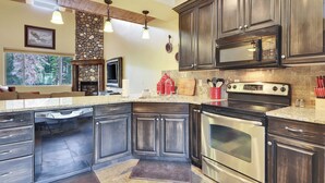 A kitchen with dark wooden cabinets, a stone backsplash, a built-in oven, and a large window overlooking a forest. - Two levels | Gas fireplace | Walk to ski slopes (Brian Head)