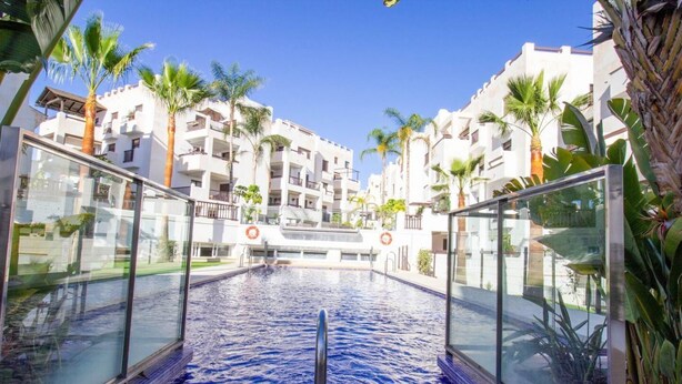 An indoor swimming pool with glass walls, surrounded by white buildings and palm trees. - Apartment Oasis of Salobreña Gym and Balcony (Granada)