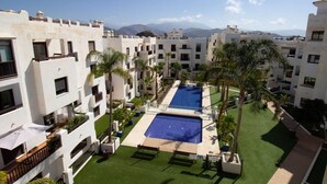 A hotel courtyard with two swimming pools, palm trees, and a view of mountains. - Apartment Oasis of Salobreña Gym and Balcony (Granada)