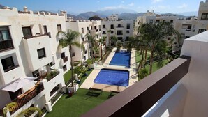 A courtyard with a swimming pool, palm trees, and a view of mountains. - Apartment Oasis of Salobreña Gym and Balcony (Granada)