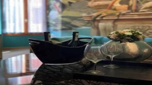 A table with a black bowl containing bottles, a vase with flowers, and two wine glasses. - Charming Canal View Apartment in Historic Venetian Palace







 (Venezia)