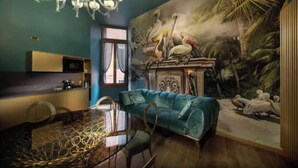 A dining area with a glass table, a blue sofa, and a mural of birds on the wall. - Charming Canal View Apartment in Historic Venetian Palace







 (Venezia)