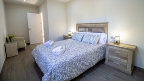 Un dormitorio con una cama grande, dos mesitas de noche, un cabecero de madera y una pequeña mesita de noche con una lámpara.