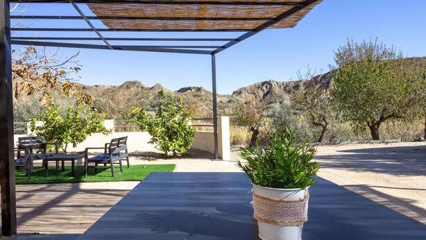 Un patio exterior con una pérgola, zona de estar y plantas en macetas.