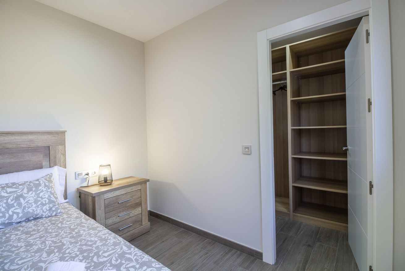 Une chambre à coucher comprenant un lit, une table de chevet, une lampe et un dressing.