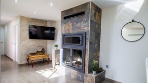 Una sala de estar moderna con chimenea de piedra, televisor de pantalla plana montado en la pared y un espejo redondo.
