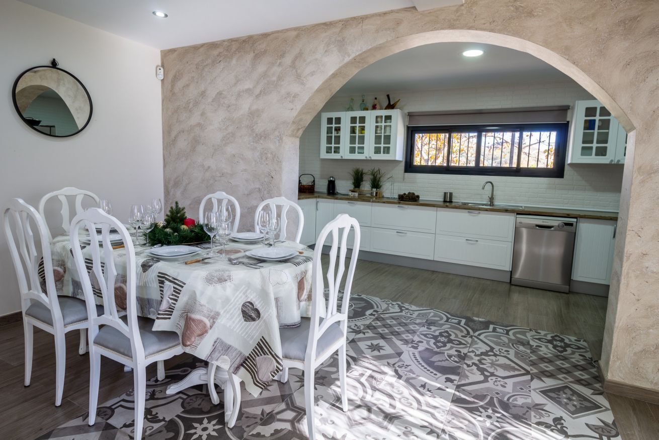 A dining area with a table set for six, white chairs, and a patterned rug.