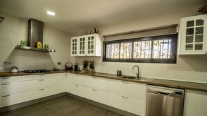 Cocina moderna con armarios blancos, lavavajillas de acero inoxidable y ventana con vistas a árboles.