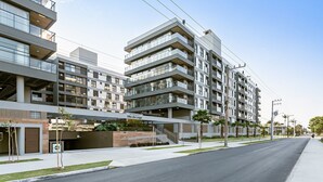Ein modernes, mehrstöckiges Wohngebäude mit Balkonen, einem überdachten Eingang und Blick auf die Straße.