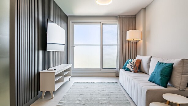 Ein modernes Wohnzimmer mit einer Couch, einem Fernseher, einer Lampe und einem großen Fenster.
