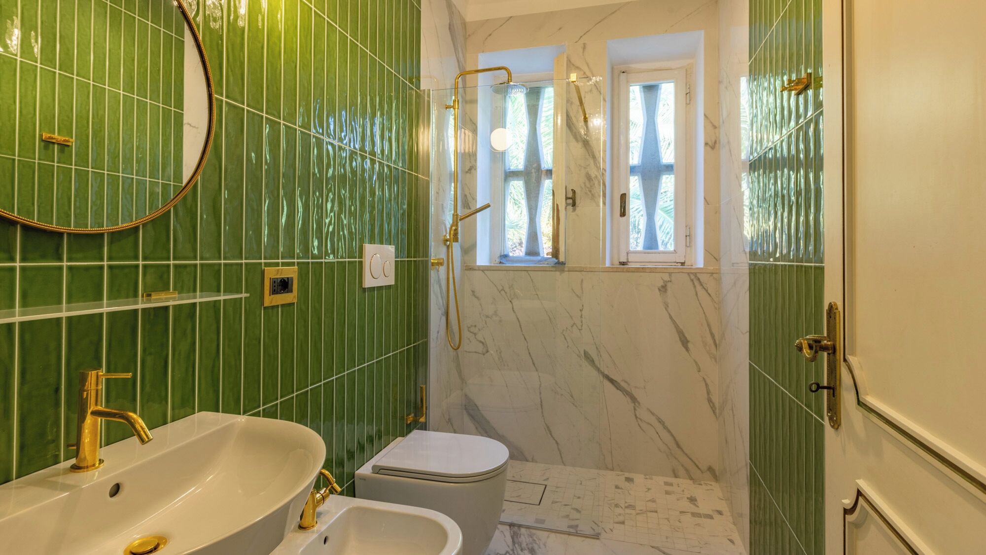A bathroom with green tiled walls, a white sink, a toilet, and a shower with a window.