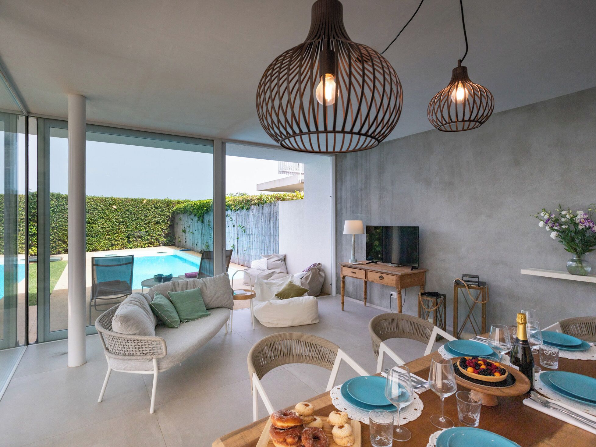A modern living room with a pool, comfortable seating, a dining area with blue plates, and a TV on a wooden cabinet.