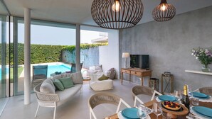 A modern living room with a pool, comfortable seating, a dining area with blue plates, and a TV on a wooden cabinet. - Villa il Melograno 4+2, Emma Villas (Ragusa)