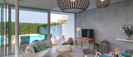A modern living room with a pool, comfortable seating, a dining area with blue plates, and a TV on a wooden cabinet.