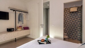 A modern hotel room with a bed, bedside table, TV, and a shower area with geometric wall tiles.