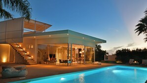 A modern house with a glass-enclosed patio, a swimming pool, and a staircase leading to the upper level.