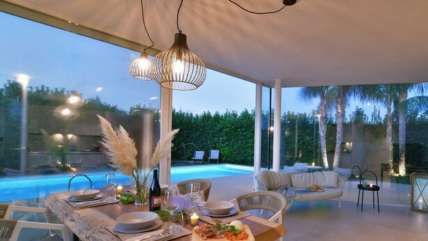 A modern dining area with a pool view, a wooden table, and a cozy seating arrangement.