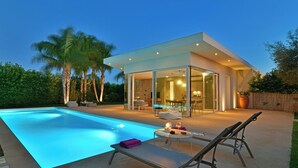 A modern house with a swimming pool, outdoor seating, and a glass-enclosed dining area.