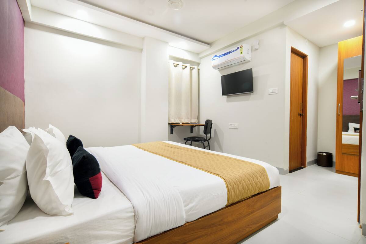 A hotel room with a bed, a TV mounted on the wall, a shower area, and a wooden door.
