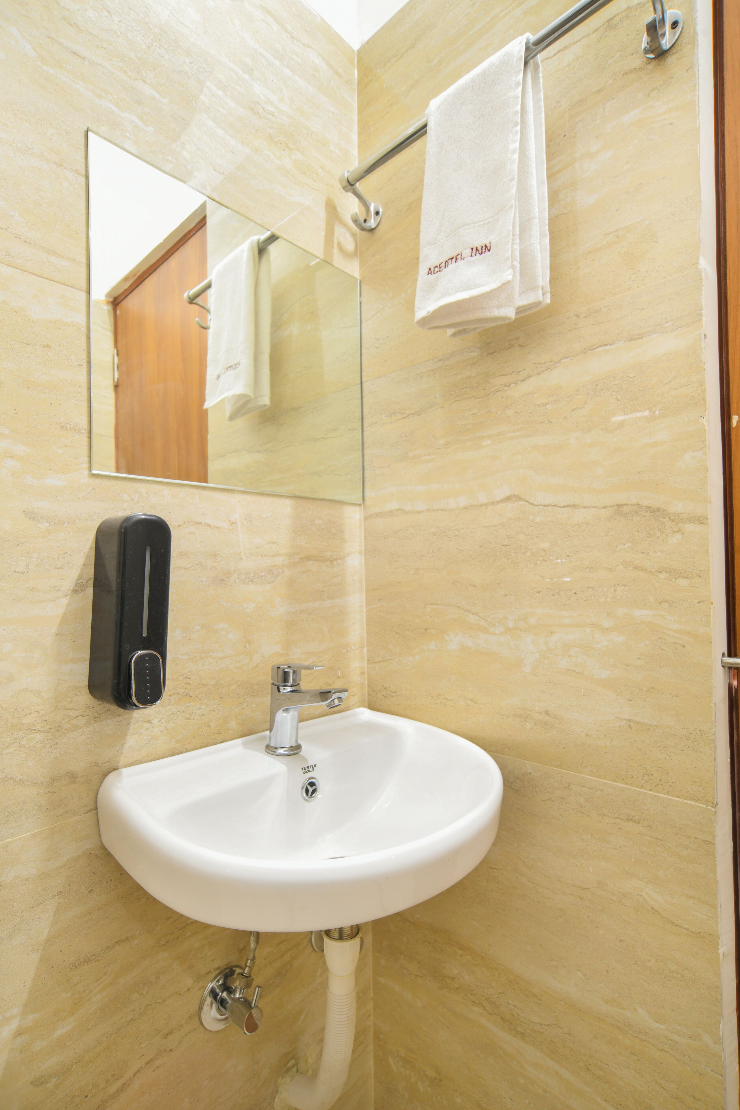 Un baño con lavamanos blanco, un espejo y un perchero con toalla.