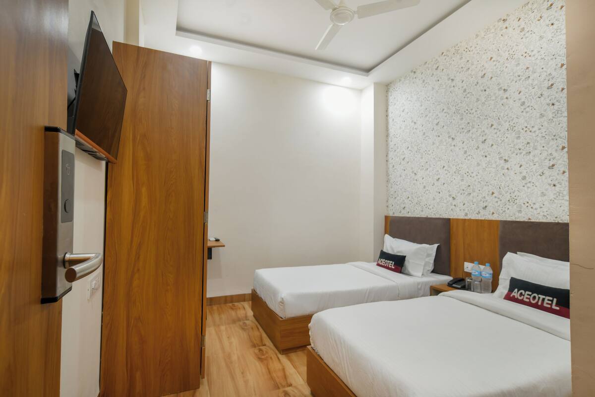 A hotel room with two beds, a wooden wardrobe, a ceiling fan, and a wall with a speckled pattern.