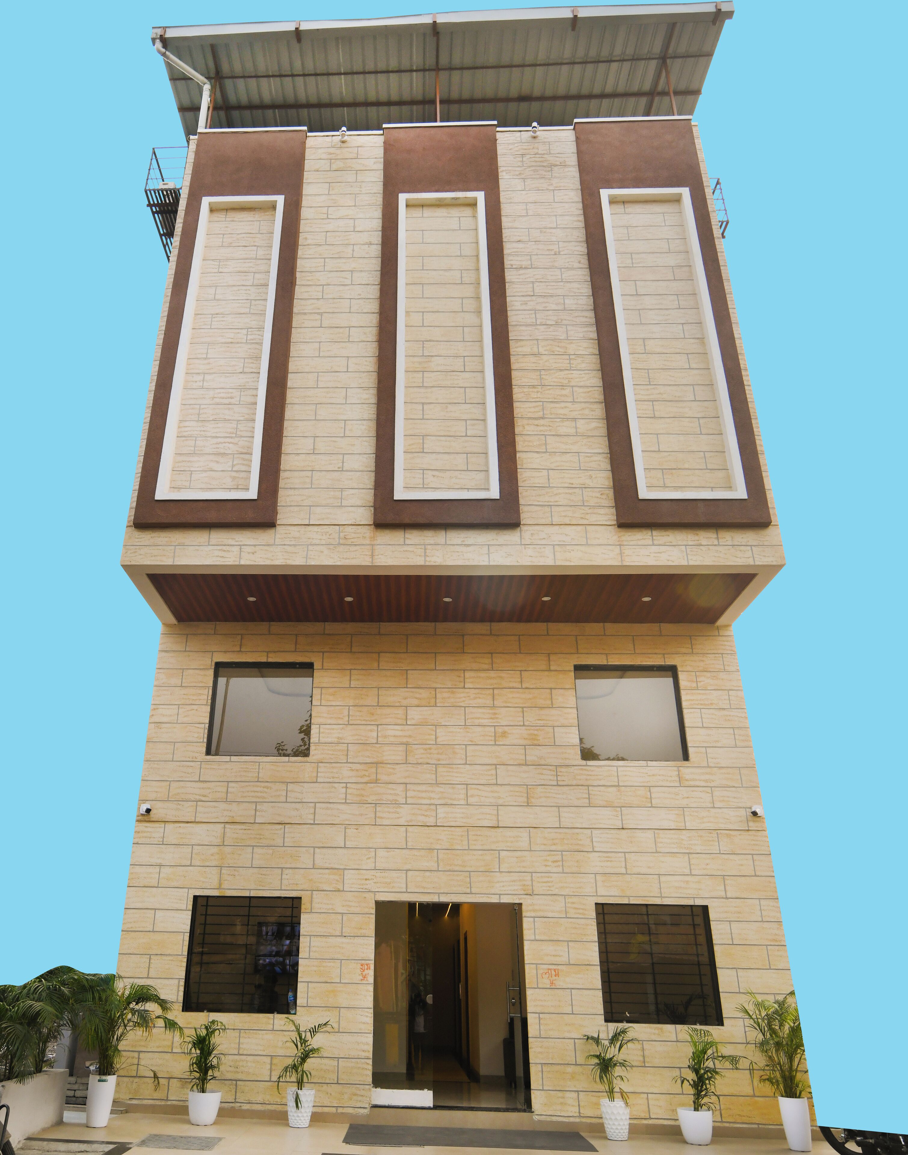 Un edificio moderno con techo plano, tres ventanas grandes con marcos marrones y una entrada central.