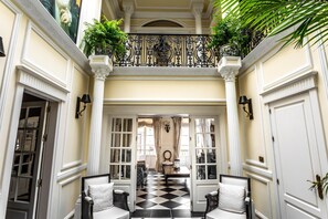 Een statige hal met een zwart-wit schachbordvloer, witte muren en een balkon met planten.