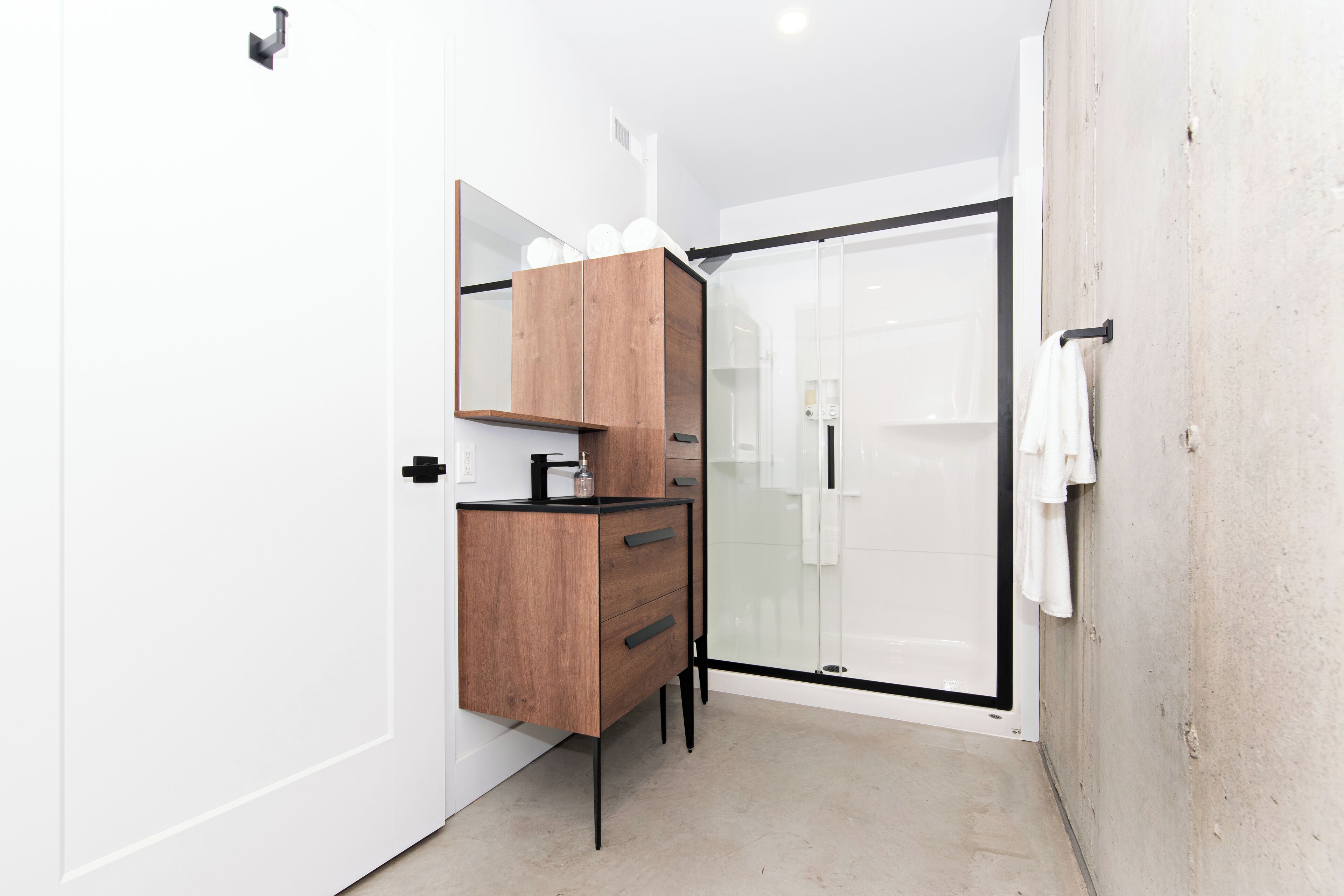A modern bathroom with a wooden vanity, a glass shower enclosure, and a white towel hanging on the wall.