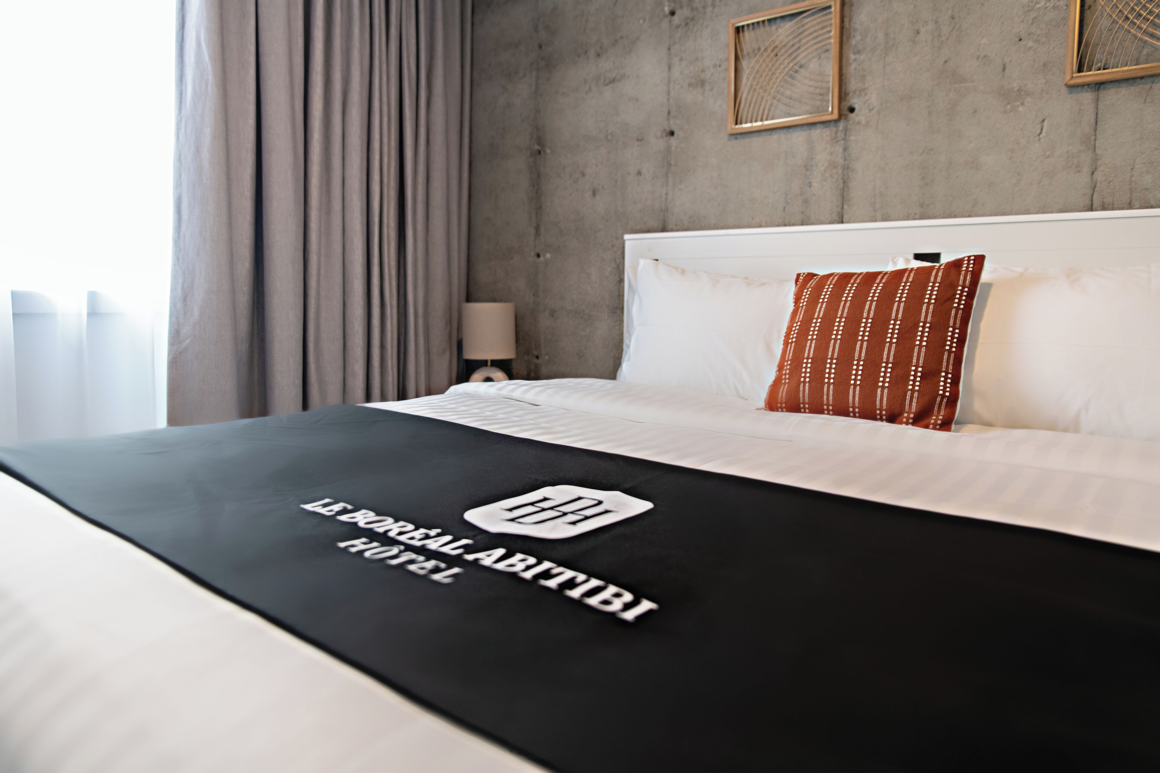 A hotel room with a bed, a nightstand, a lamp, and a window with curtains.