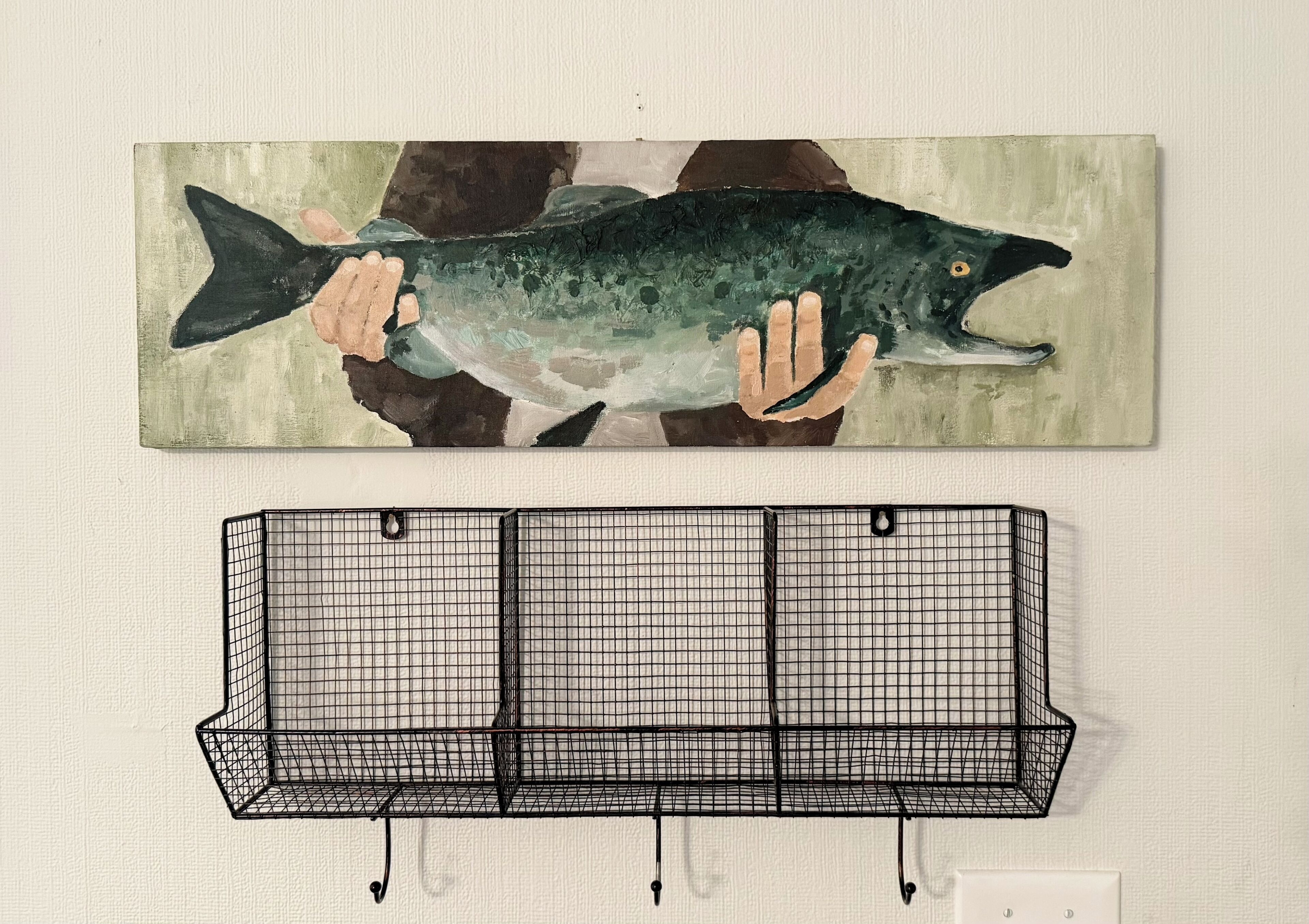 Uma obra de arte na parede, com um peixe e uma prateleira de metal preto.