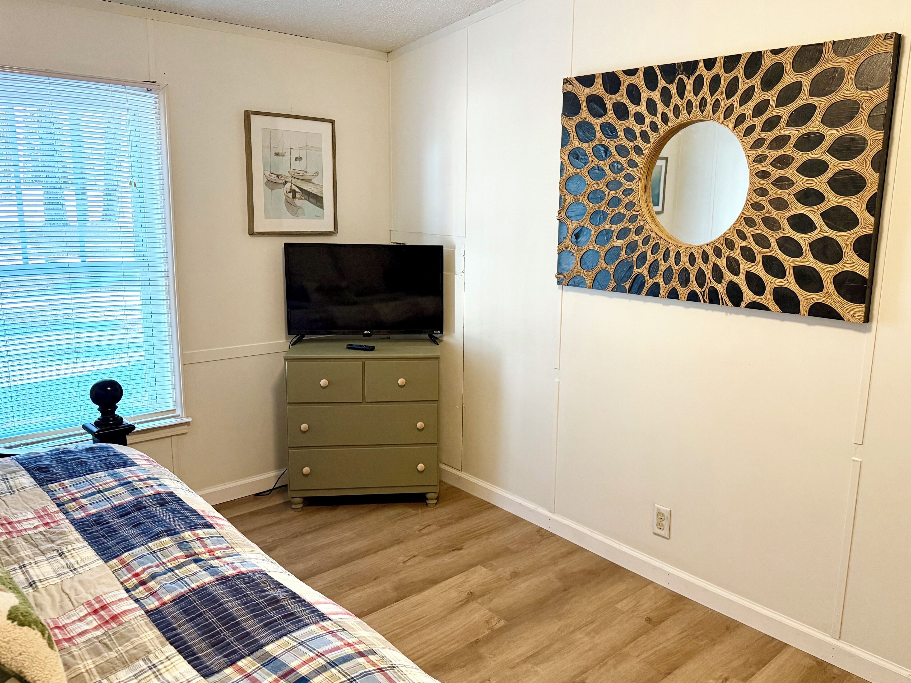 Une chambre à coucher comprenant un lit, une commode, un téléviseur, un tableau encadré et un miroir décoratif accroché au mur.