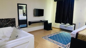 A hotel room with a large bed, a sitting area with a TV, a bathroom with a bathtub, and a window with curtains. - Great Western Hotel and Suites (Owerri)