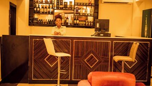 A reception area with a wooden reception desk, two white bar stools, and a red chair. - Great Western Hotel and Suites (Owerri)