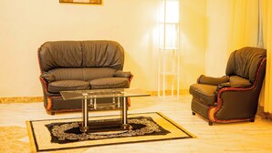 A living room with a sofa, a chair, a glass coffee table, a floor lamp, and a patterned rug. - Great Western Hotel and Suites (Owerri)