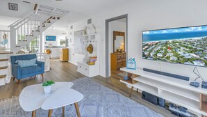 A modern living room with a large TV, a staircase, and a view of a coastal area. - Reese's Beach Retreat on beautiful Anna Maria Island (Holmes Beach)
